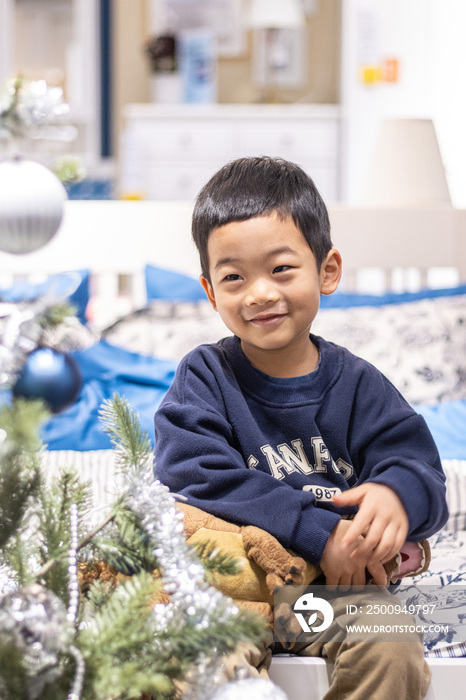 一个小男孩抱着毛绒玩具坐在圣诞树旁