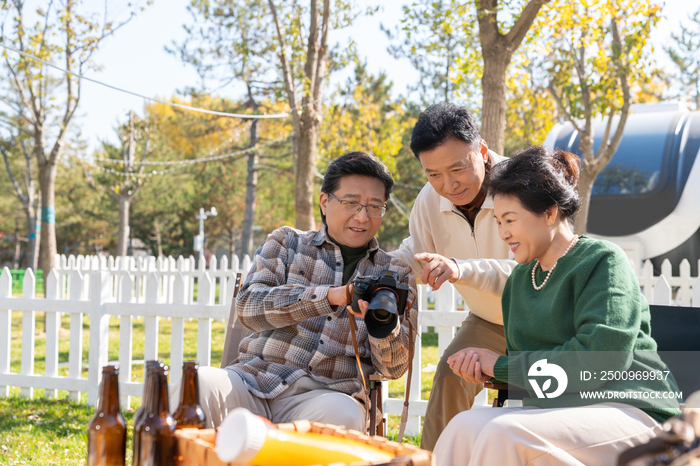 一群中老年人坐在露营地看数码相机