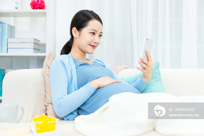 年轻孕妇在沙发上使用手机