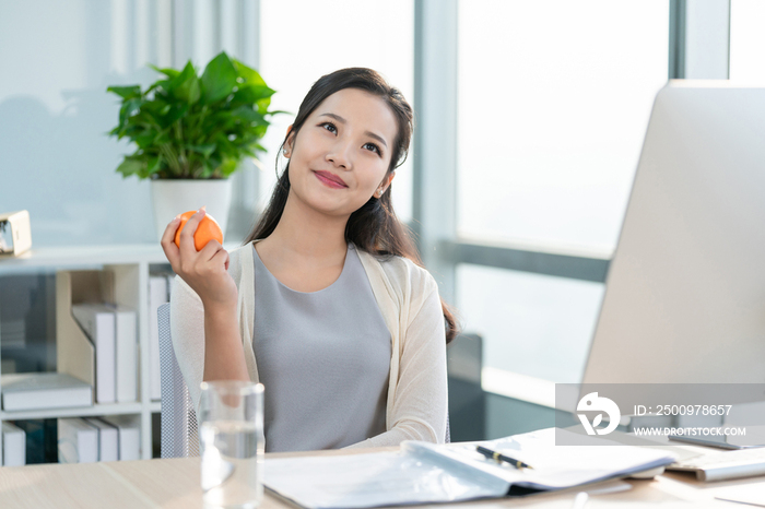 年轻女子在办公室拿着一个橙子