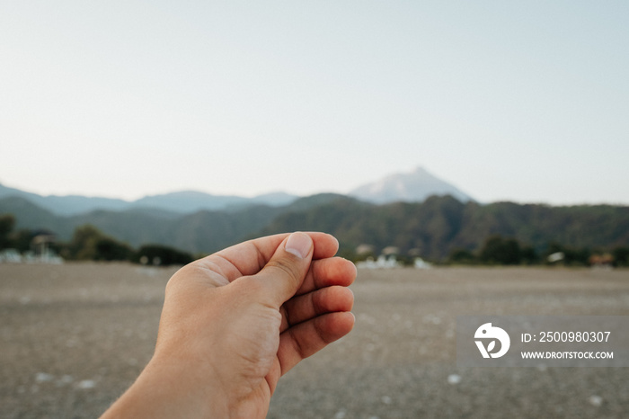 A hand simulates holding a photo, postcard or note on beautiful sunset over the mountains at the beach in summer day.