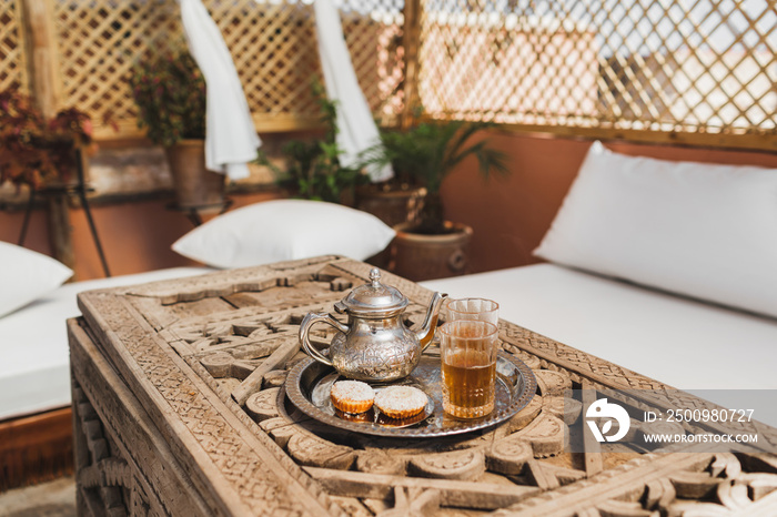 Traditional moroccan mint tea with cookies on silver tray on carved wooden table. Beautiful vintage style, hospitality in Morocco.