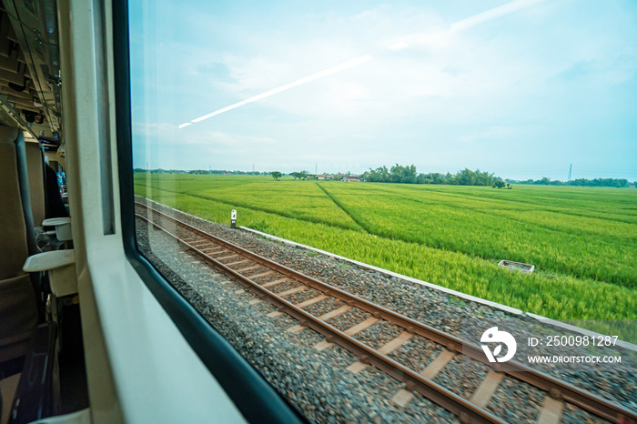 Riding a train in Indonesia sitting by the window watching the tracks and the view outside the window of the train speeding towards its destination