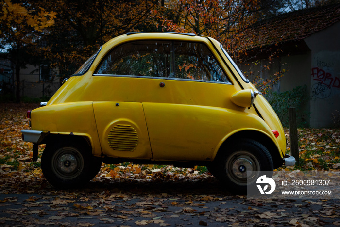 A tiny yellow old car car in autumn