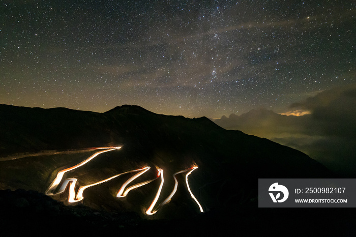 Car driving down the mountain pass road under a starry sky, Stelvio, italian alps. Composite of several frames.