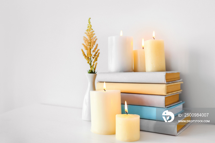 Composition with beautiful burning candles and books on table