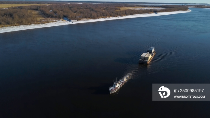 Aerial view of a barge floating on a wide river past the autumn meadows. Clip. The cargo ship carrying goods at a navigable river.