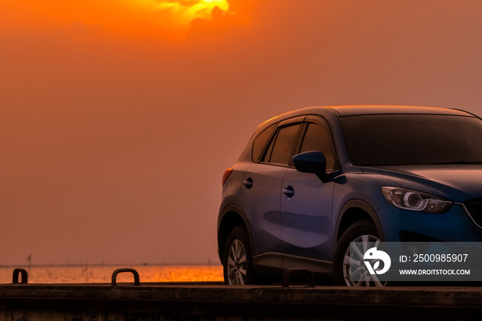 Blue compact SUV car with sport and modern design parked on concrete road by the sea at sunset in the evening. Hybrid and electric car technology concept. Car parking space. Automotive industry.