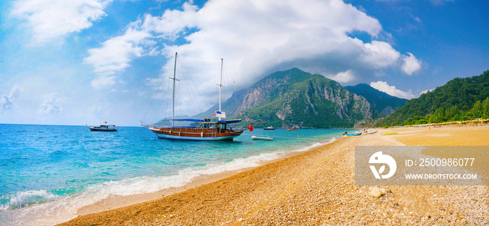 Beautiful panoramic view of sea and beach Cirali, Kemer, Antalya, Turkey. Ship against backdrop of mountains and blue sky with clouds on sunny day.