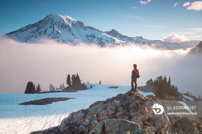 Man on the mountain peak looking on mountain valley with low clouds at colorful sunrise in autumn in Mount Rainier National park, Washington, USA. Landscape with traveler, foggy hills. Alone tourist