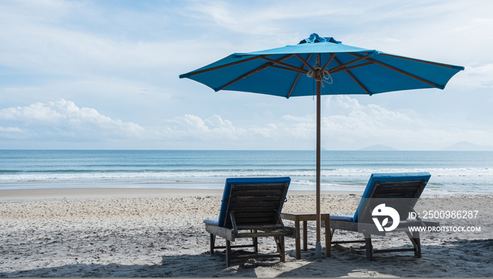 Beach chairs and umbrellas on the sand beach with cloudy blue sky background. Summer vacation travel concept.