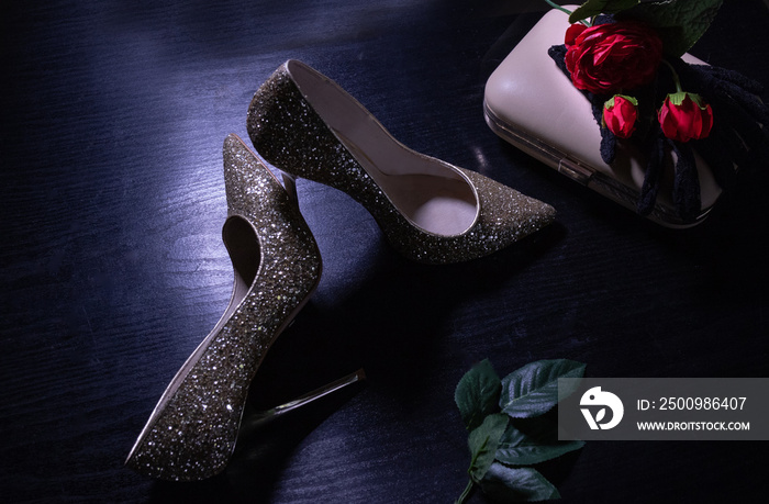 gold high-heeled shoes close-up on a dark table with a clutch bag and gloves