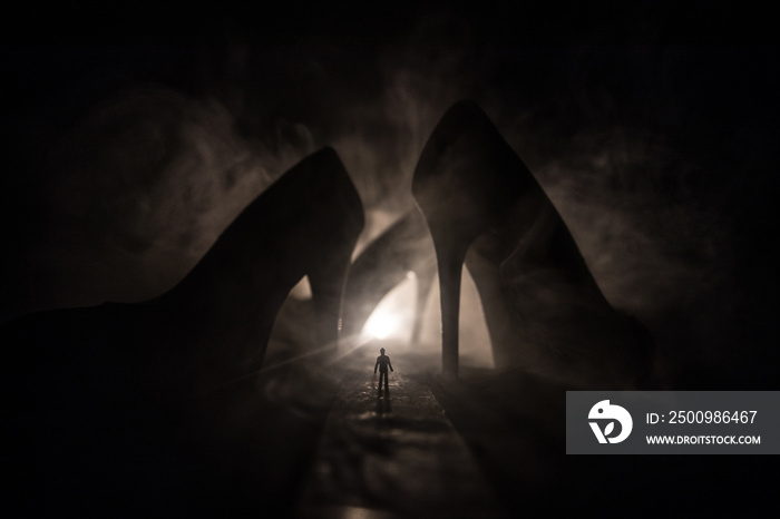 Artwork decoration. Silhouette of a man standing in the middle of the road on a misty night with giant high heel women shoes. Women power or women domination concept.