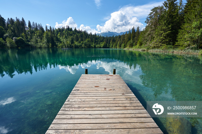 Landscape panorama of Crestasee - Lake Cresta in June, municipalities of Flims and Trin in the Grisons, Switzerland. Wooden dock on the lake.