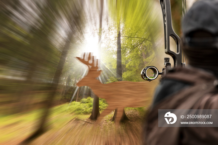 An archer, with his compound bow (hunting bow) aims at a silhouette of a fake wooden deer in the woods.