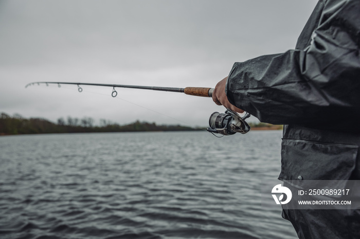 Fishing rod with a spinning reel in the hands of a fisherman on an overcast spring day. Fishing background.