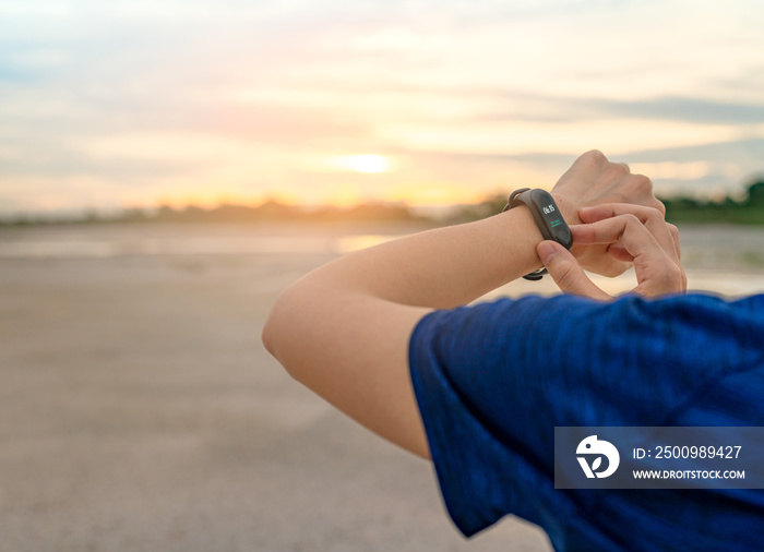 Young Asian woman touching smart band after running in the morning. Wearable computer. Heart rate monitor bracelet. Fitness device. Activity or fitness tracker. Smart watch connected device. Wristband