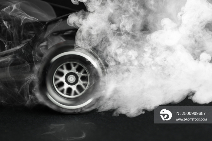 Modern racing car with smoke from under wheels on dark background, closeup
