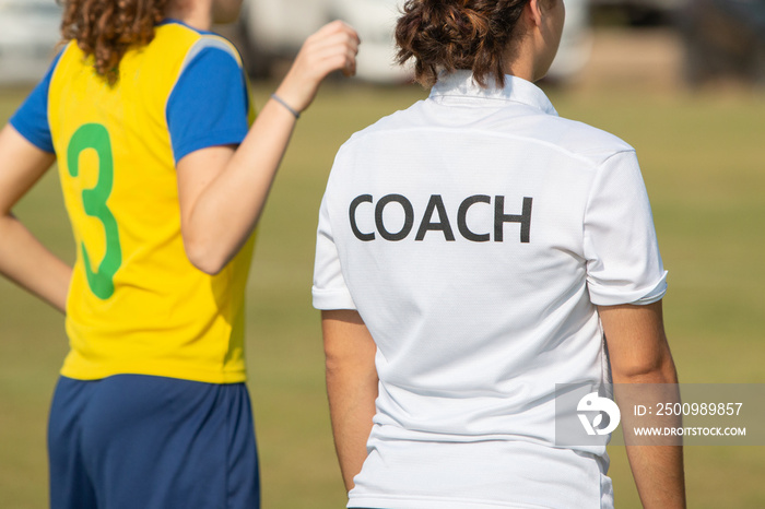 Back of sport coach wearing COACH shirt at an outdoor sport field