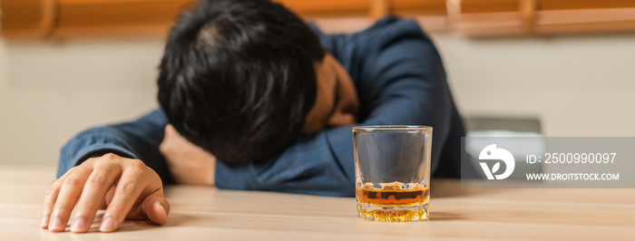 Alcoholism, depressed asian young man sleep on table while drinking alcoholic beverage, holding glass of whiskey alone at night. Treatment of alcohol addiction, suffer abuse problem alcoholism concept