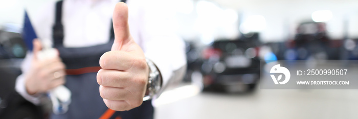 Close-up of person showing thumbs up. Good job and well done symbol. Copy space in right side. Mechanic in uniform posing in garage. Repair service station and handyman concept