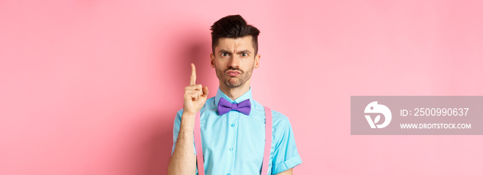 Angry male teacher shaking finger and scolding someone who misbehave, frowning grumpy, and teaching lesson, standing over pink background