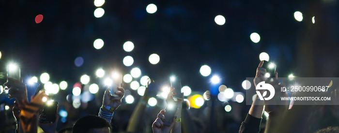 raised hands with smartphone lights during concert - blurred image