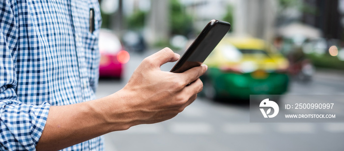 Young man tourist or casual businessman ordering taxi via cab application on smartphone in city street, Male traveler using mobile phone and Searching direction on digital map at Bangkok, Thailand