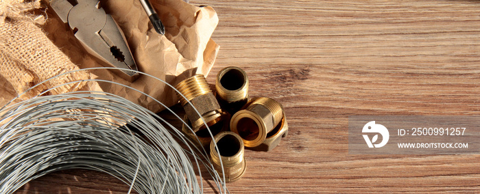 Pipe adapters, screwdriver, pliers and wire on a wooden background.