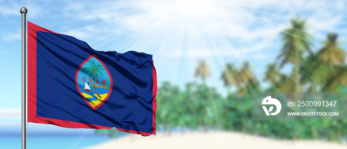 Waving Guam flag in the sunny blue sky with summer beach background. Vacation theme, holiday concept.