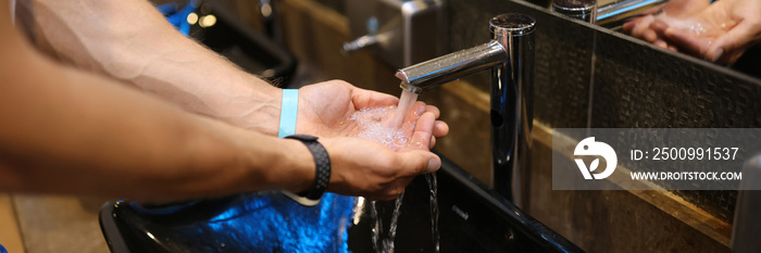 Man washes hands in the sink in bathroom at home checking temperature by touching running water with hand