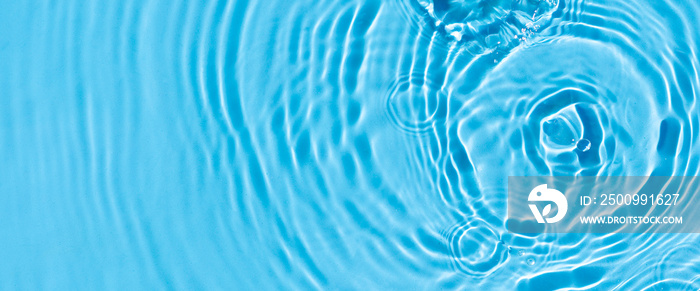 Wave from a drop of water on blue water under natural light. Top view, flat lay.