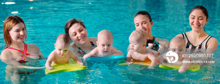 A group of mothers with their young children in a children’s swimming class with a coach.