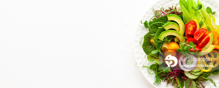 Delicious healthy salad of fresh avocado, tomatoes, cucumbers, peppers, lettuce, microgreens on white plate. Clean eating, lunch bowl. Top view.