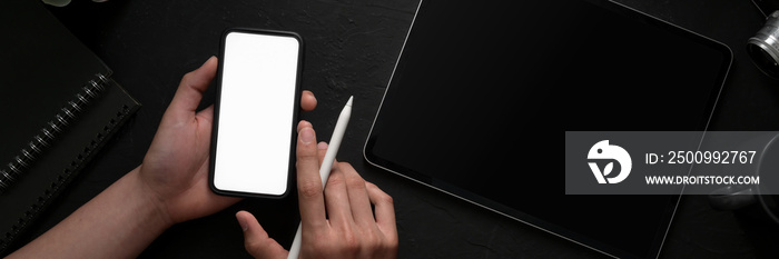 Overhead shot of a man holding blank screen smartphone in dark modern concept workspace