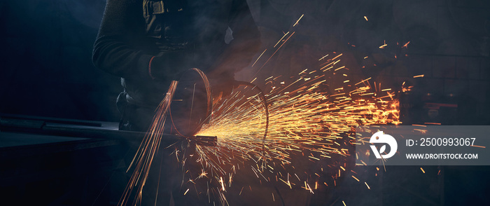 Young man grinding metal on steel pipe with flash sparks.