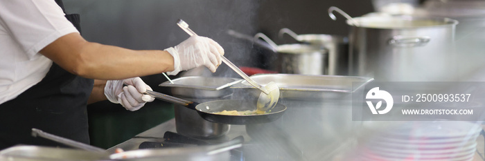 Cook prepares food in frying pan in kitchen