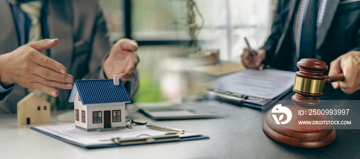 Lawyer or businessman sitting at table with fair scales Hammer and small wooden toy house work with documents Sign a contract agreement Real estate law, auction house concept