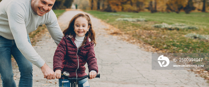 Lovely little girl learning to ride a bicycle with her father outdoor in the park.