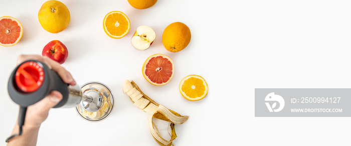 Female hands use a hand blender to mix fresh fruits to make a diet smoothie on a white background. Top view, flat lay. Banner