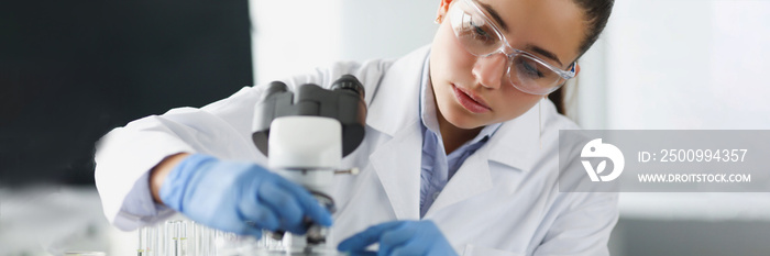 Woman scientist chemist in protective glasses putting glass slide in microscope in laboratory