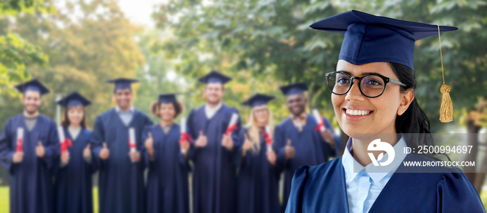 education, graduation and people concept - happy female graduate student in mortarboard and bachelor gown over group of classmates in summer park background