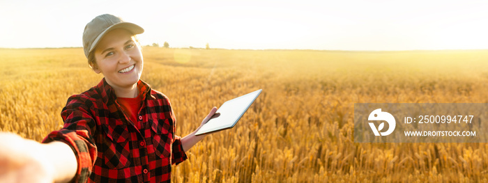 Woman farmer with digital tablet makes selfie on the background of a wheat field.