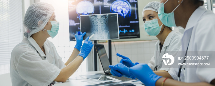 Team of female doctor check on scan results paper and looking at monitors in laboratory and plan and share medical knowledge and experience benefits her coworkers and patients