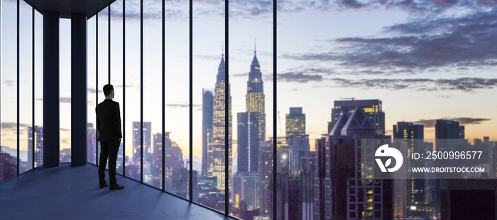 Businessperson in empty office looking out of panoramic window with bright city downtown and sky view with mock up place. Future, tomorrow, perspective and career concept.