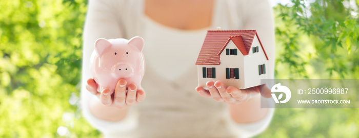 mortgage, investment, real estate and property concept - close up of woman holding home or house model and piggy bank over green natural background