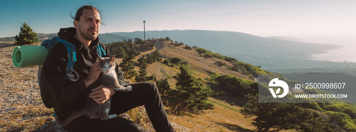 A male tourist meets a dawn in the mountains. Hiking. The cat travels with a man in the mountains at dawn