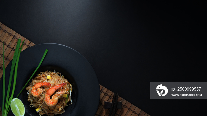 Overhead shot of Pad Thai, stir fly of Thai noodle with shrimp and egg in black ceramic plate on bamboo placemat