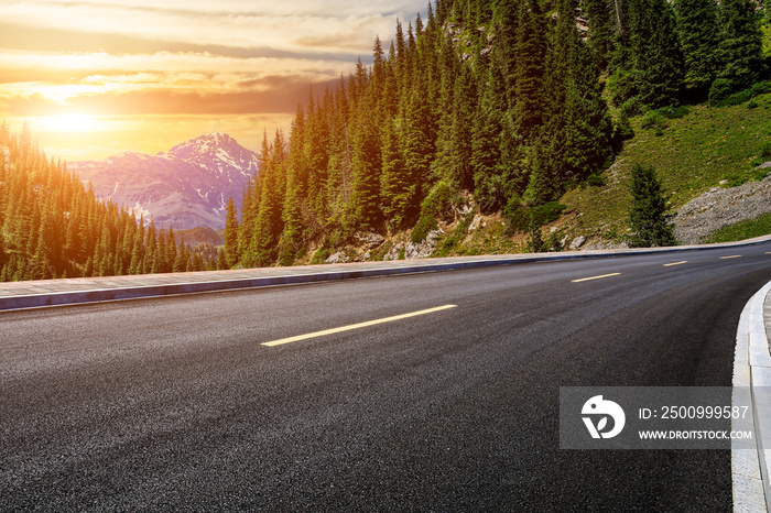 Asphalt road and green forest with mountain natural scenery at sunset in Xinjiang, China.