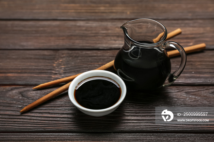 Bowl and jug of soy sauce with chopsticks on dark wooden background